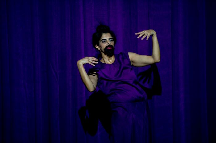 Une femme à barbe danse seule devant un rideau violet