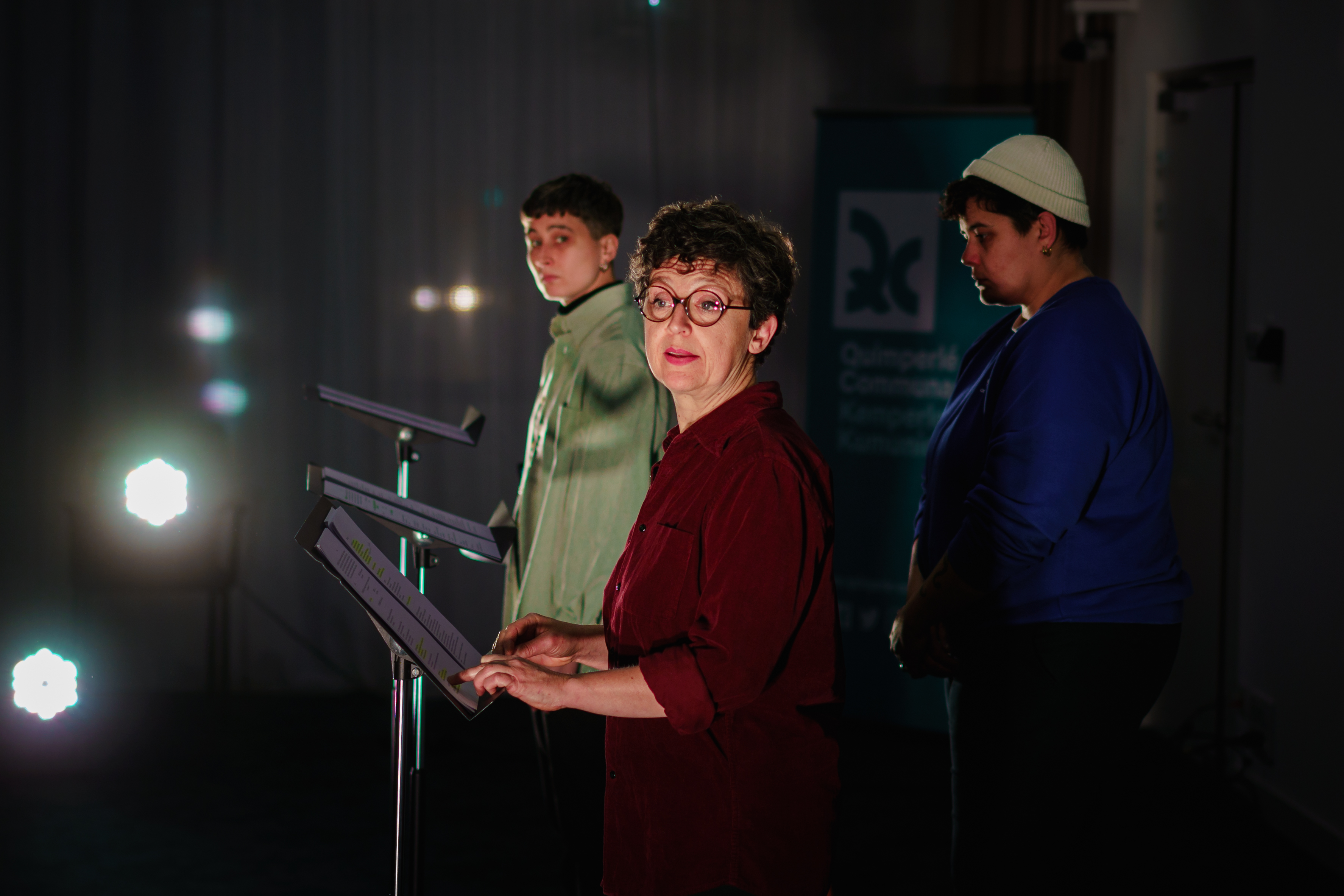 3 femmes devant un micro sur scène, vue de profil, deux d'entre elles regardent vers l'objectif