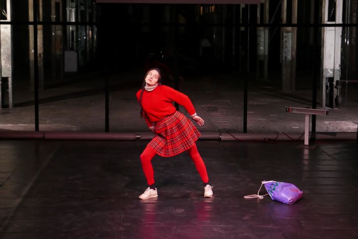 La comédienne est au centre de la scène en rouge. Elle se penche côté droit.