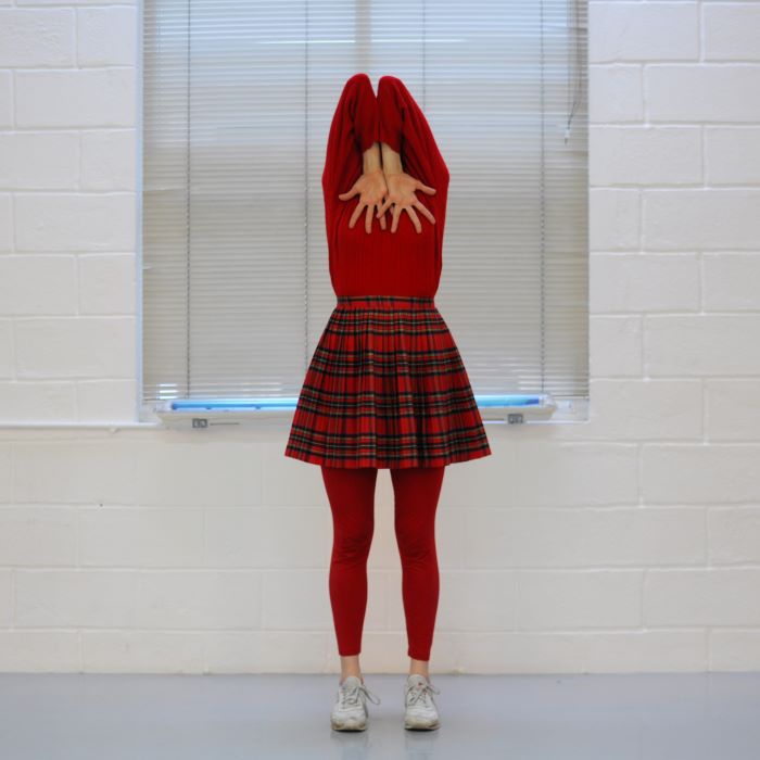 La comédienne est face à l'objectif mais cache son visage avec ses bras repliés e les mains bien écartées.