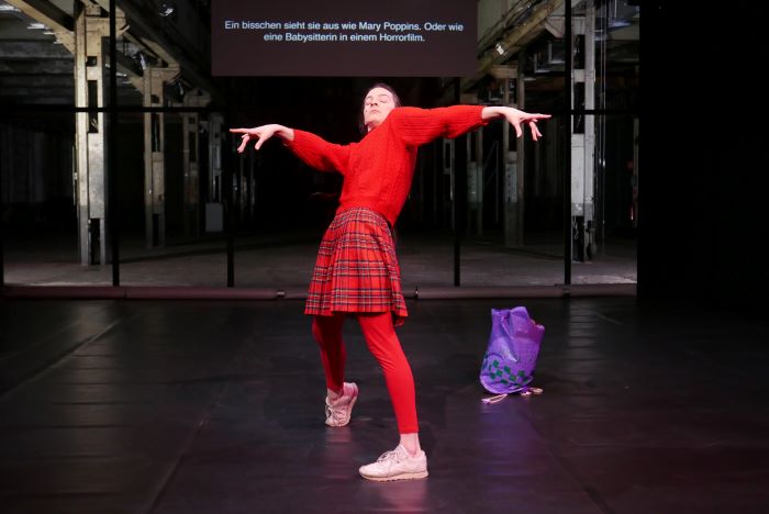 La comédienne est au centre de la scène et se penche vers l'arrière les bras tendus sur les côtés. Elle est habillé en rouge.