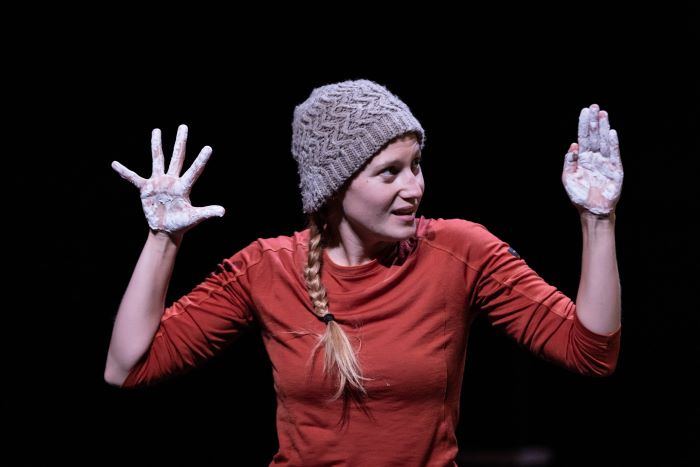 La comédienne est face au public et montre ses mains recouvertes de matière blanche.