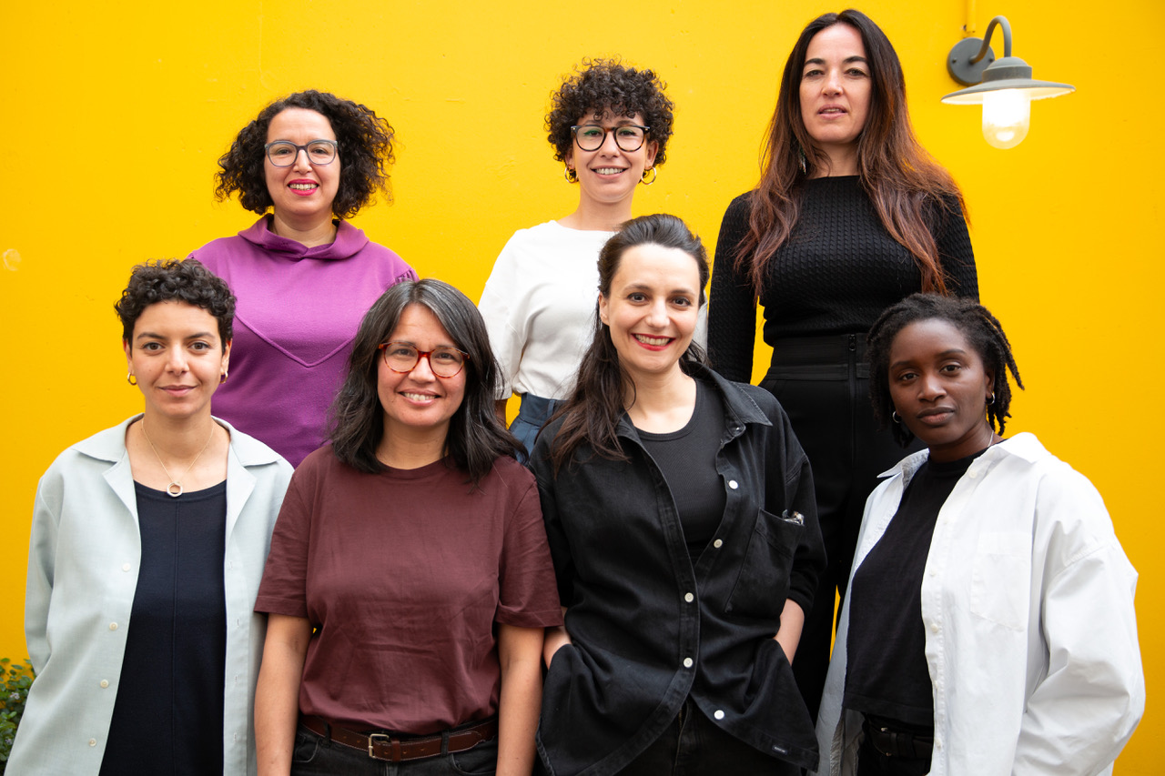 Sept femmes posent ensemble sur un fond jaune.